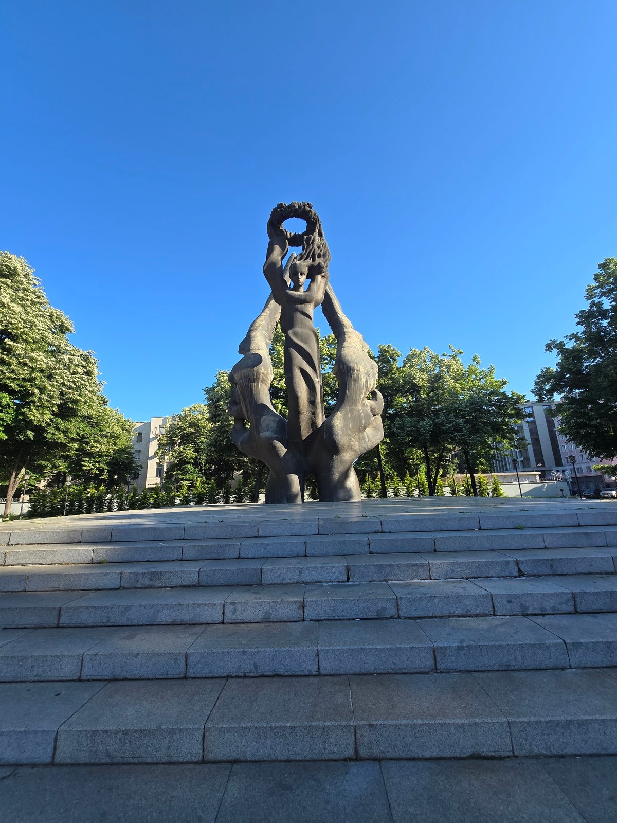 Bronze Monument With Wreath-Holding Figures Observed Against Clear Skies