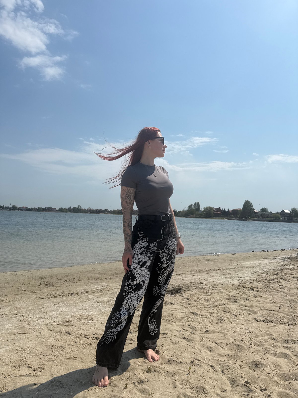 Woman in dragon-patterned pants gazes skyward on beach