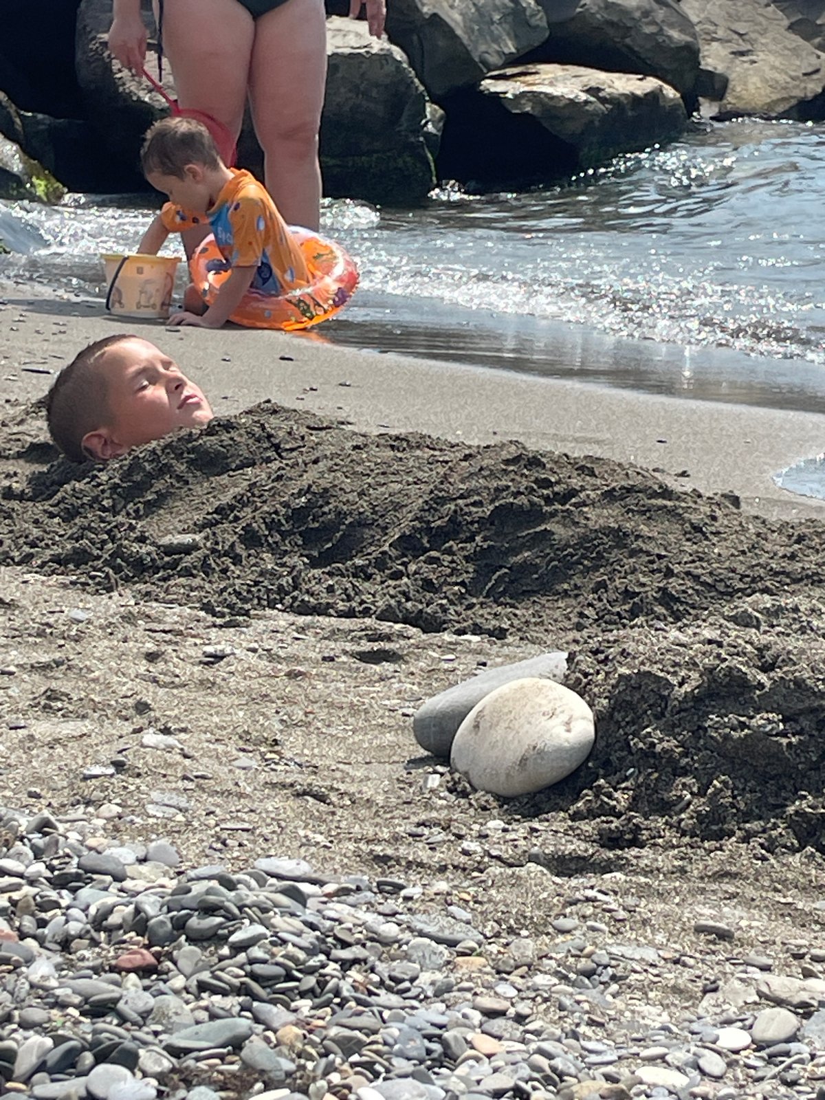 Kids playing on a Sochi beach, one buried in sand