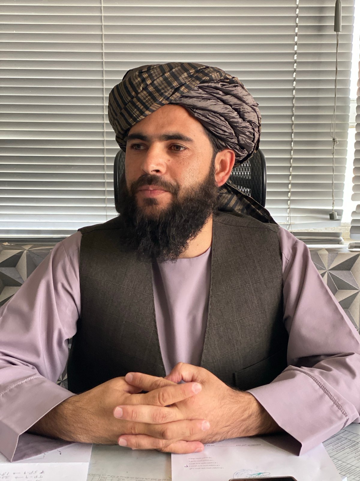 Seated at a desk in Kandahar, hands clasped, formal posture.