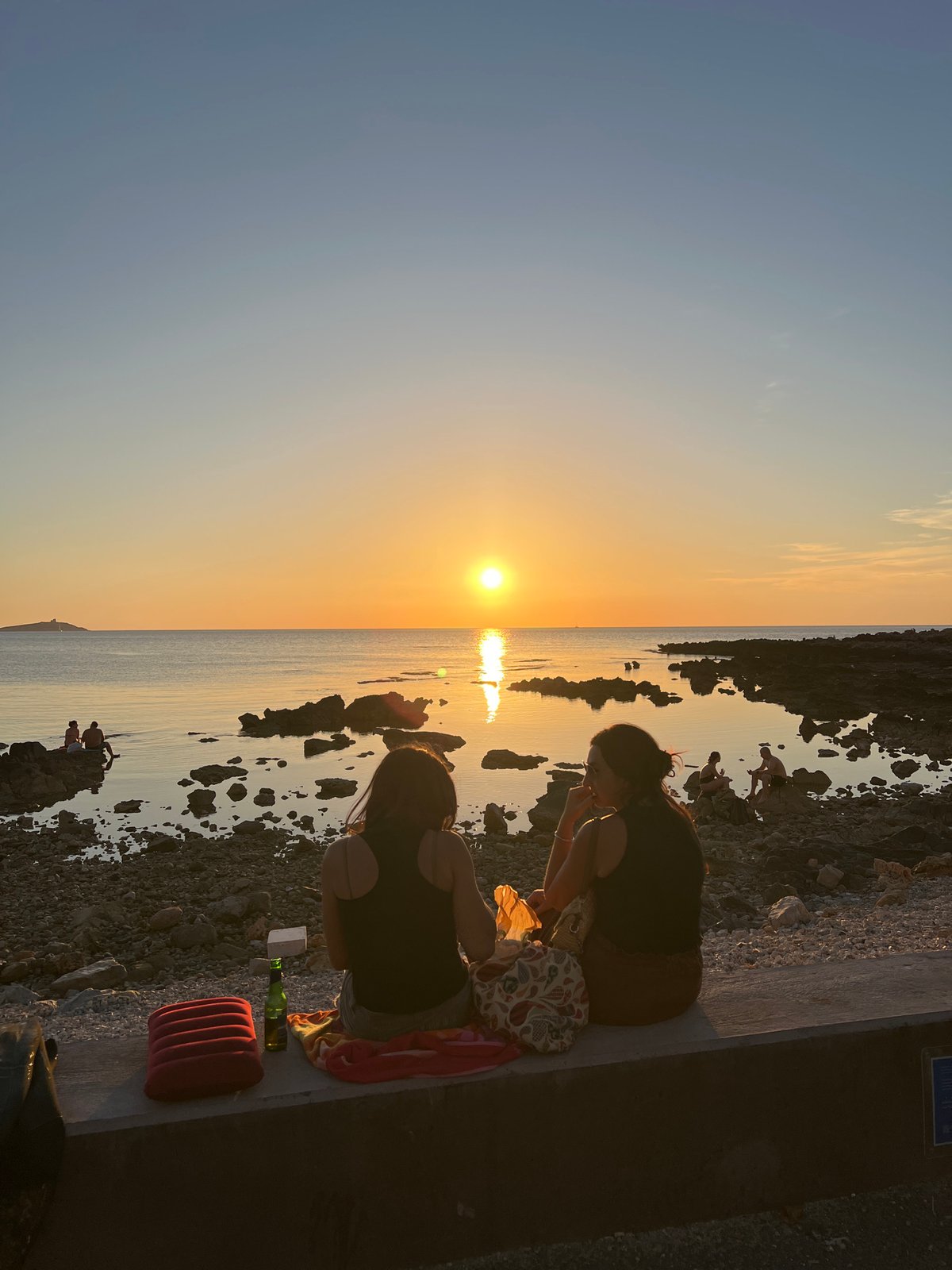 Golden hour on a rocky Palermo coastline, people unwinding at sunset