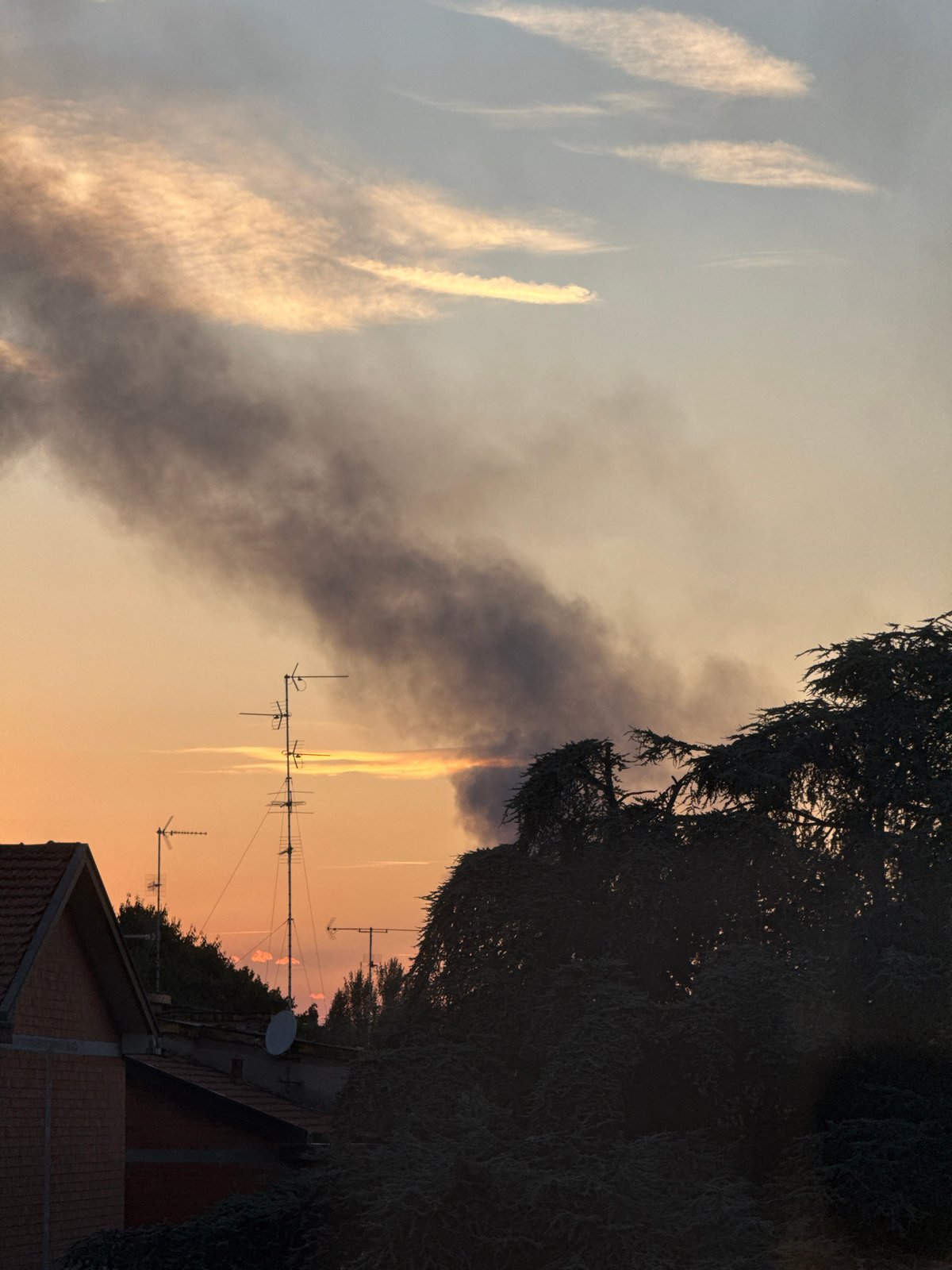 Dark smoke rises over Milan skyline at sunset