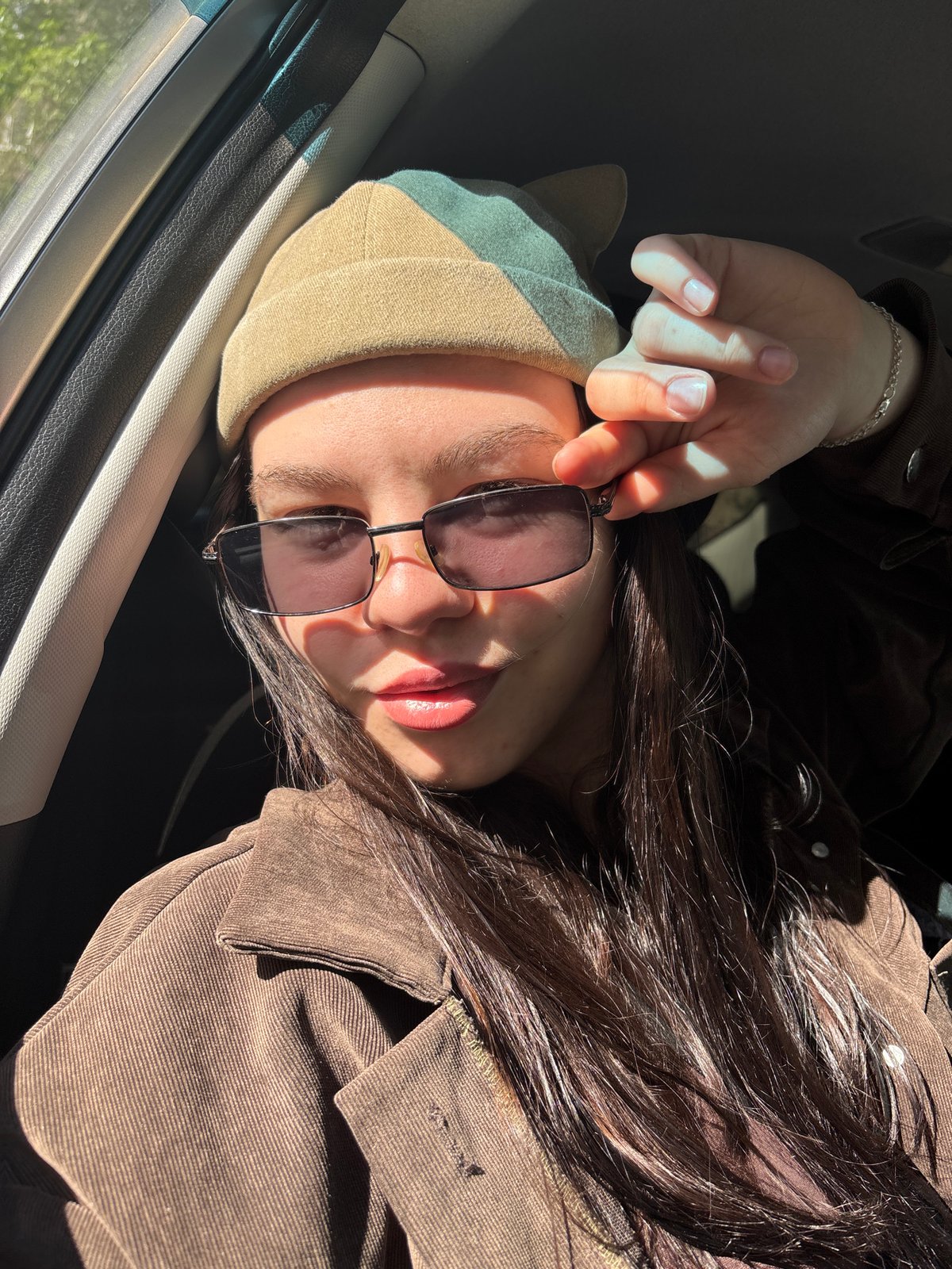 Woman adjusts sunglasses in car during sunny morning in Perm