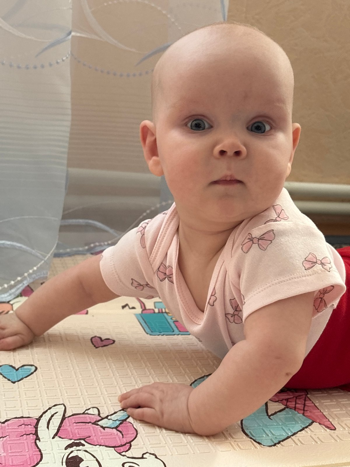 Baby in pink onesie plays on mat in Votkinsk