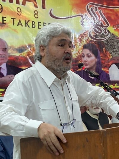 Grey-bearded man addresses formal indoor political gathering