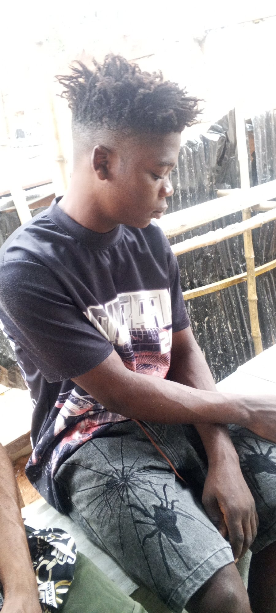 Young man sits quietly in patterned shirt, grey shorts