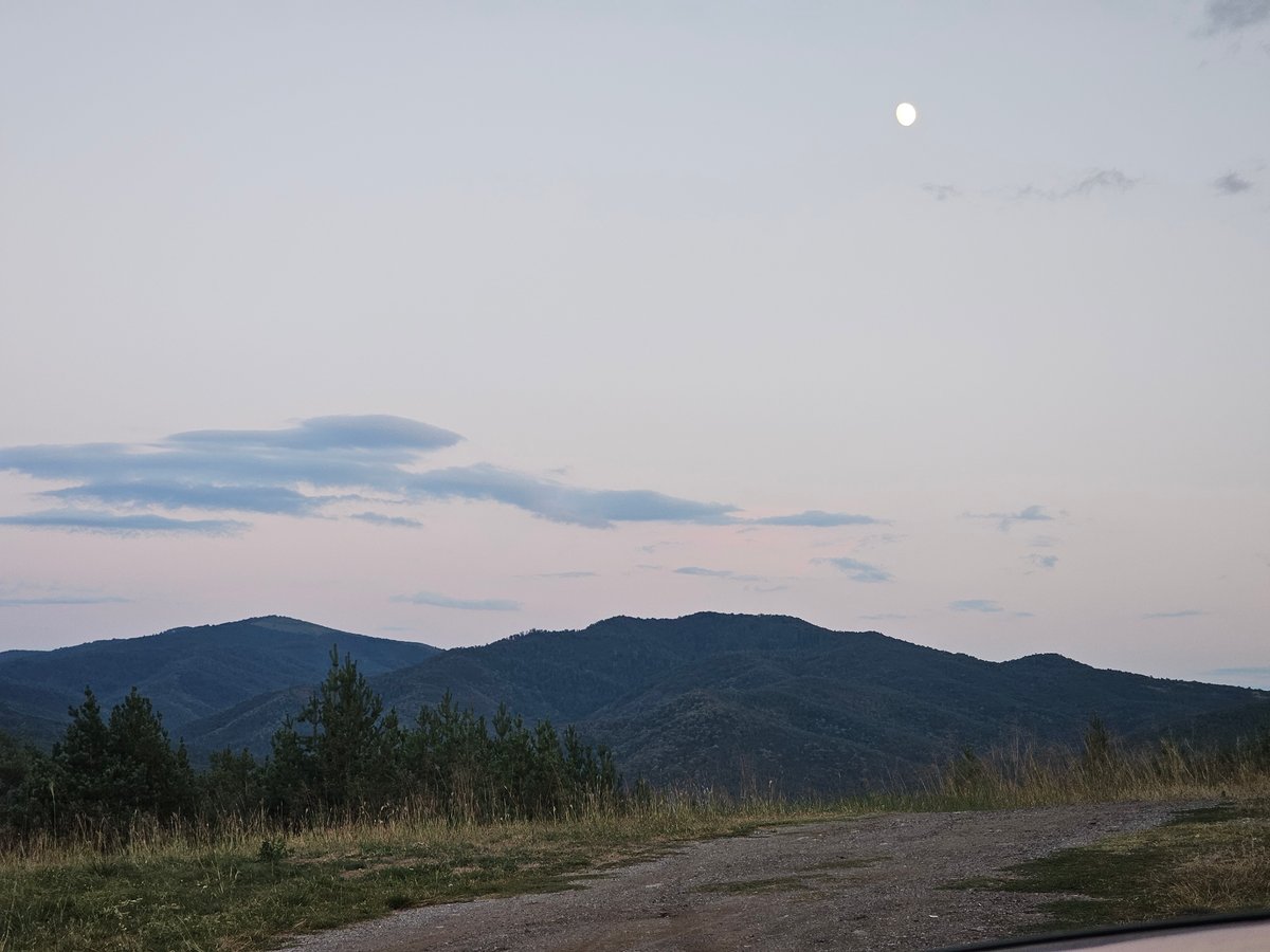 Moon rising over mountains, modern building in the foreground at dusk