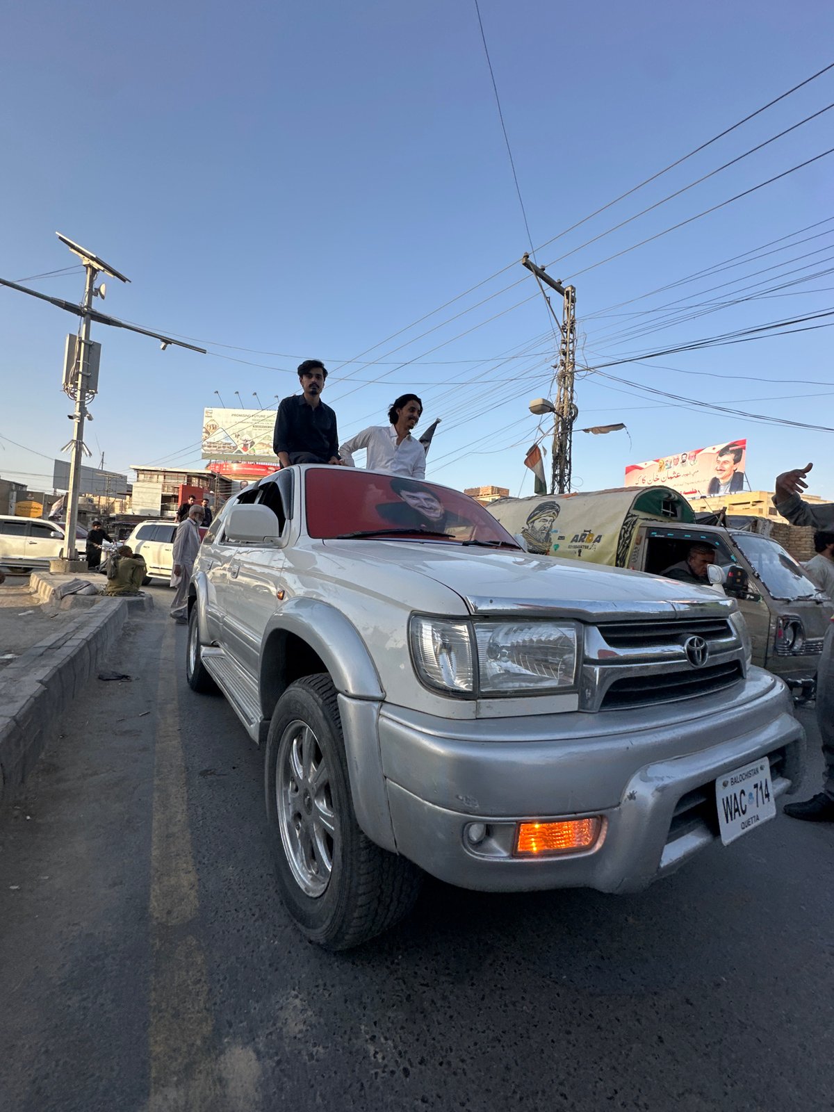 Flag-draped vehicle procession winds through Quetta at sunset