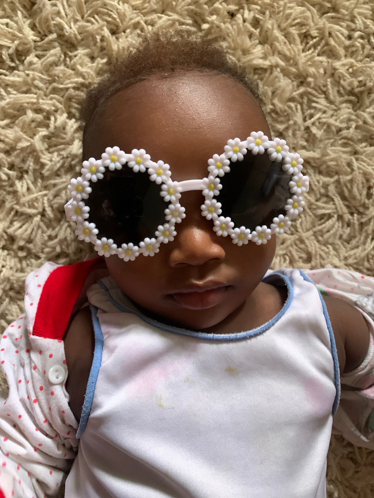 Baby in flower sunglasses photographed on carpet in Nigeria