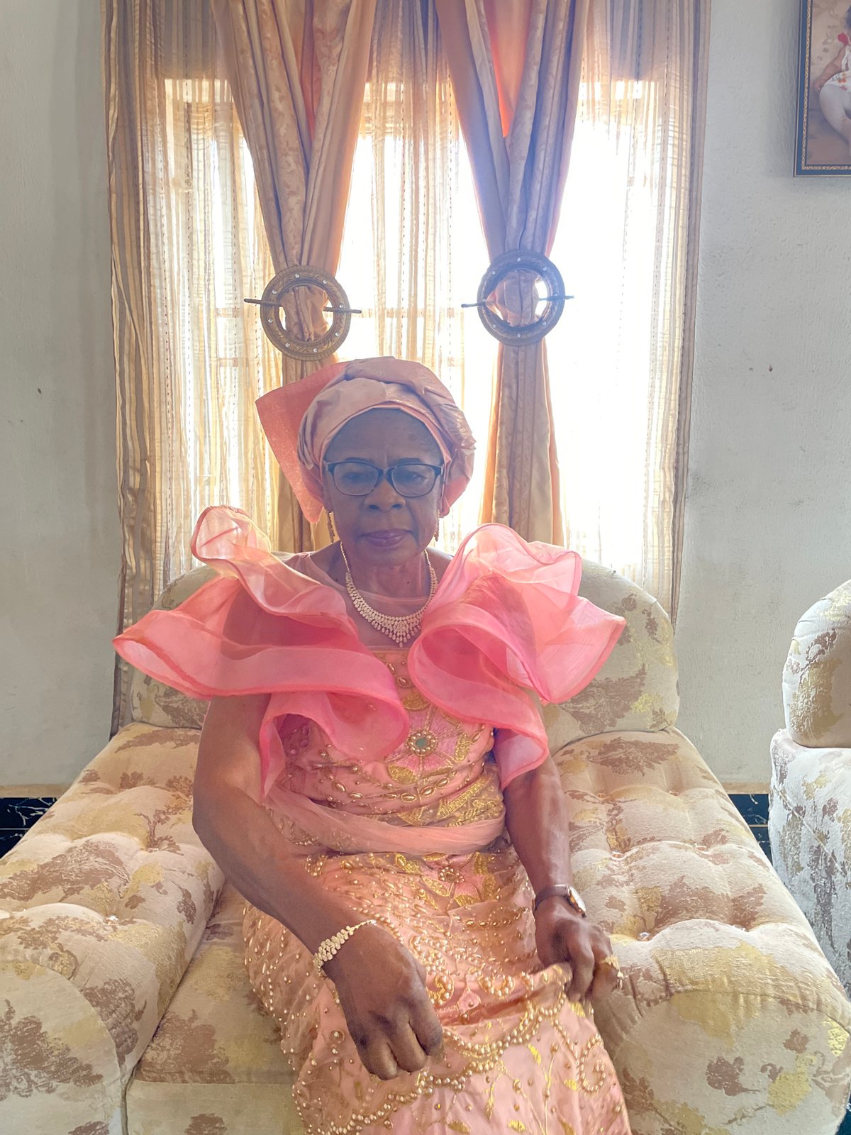 Elderly woman in pink dress photographed on patterned sofa