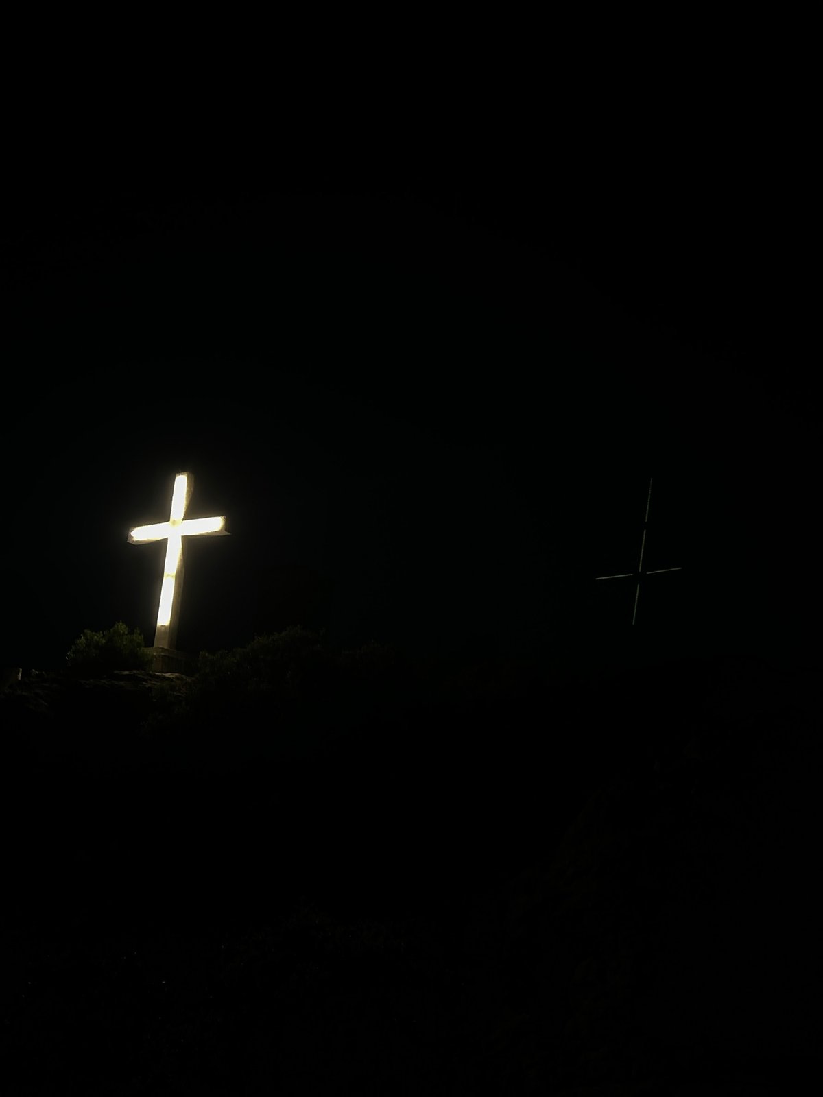 Illuminated hilltop cross overlooks a glowing coastal city at night