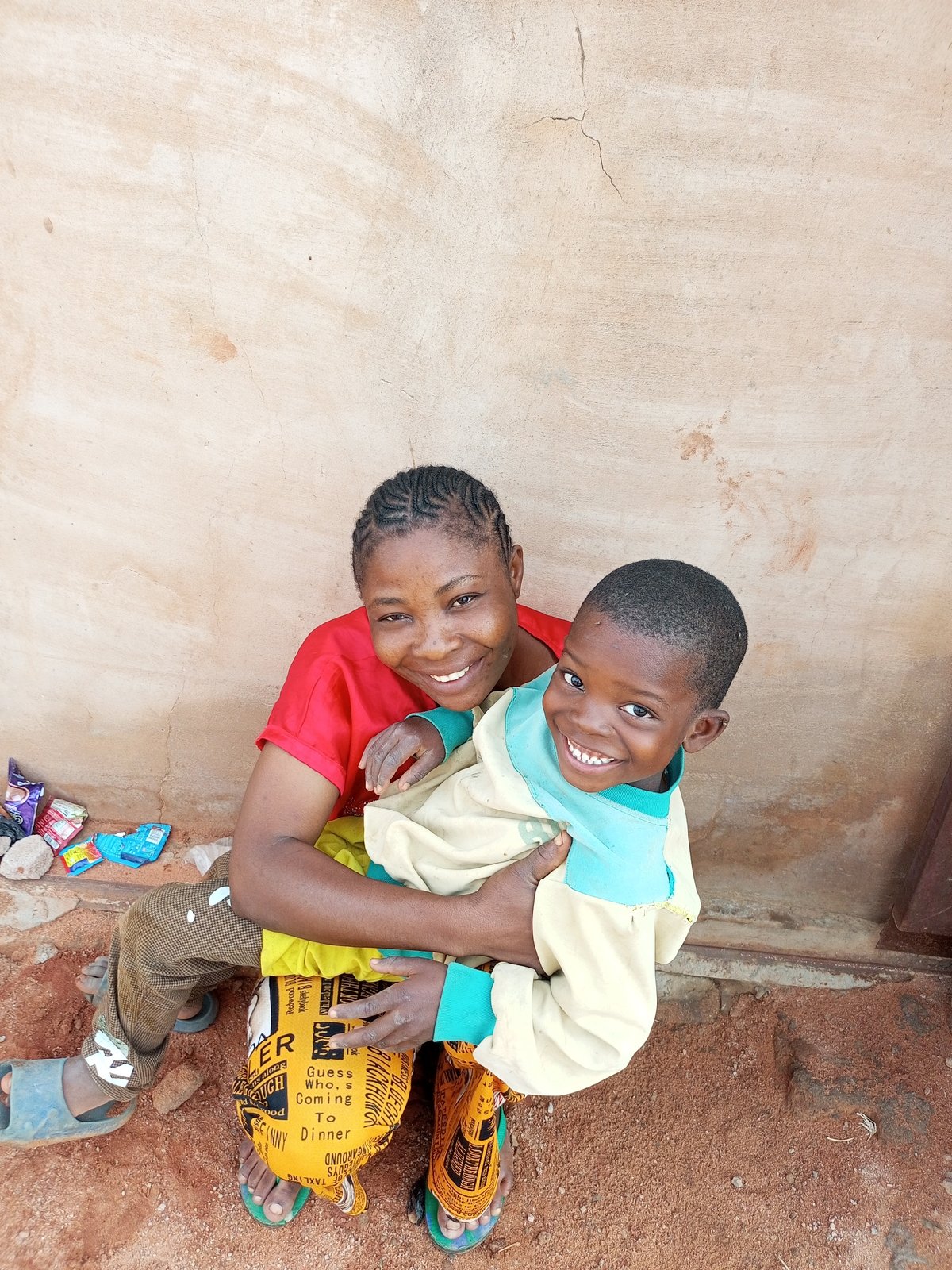 Braided hair, bundled child, warm smile by a tan wall