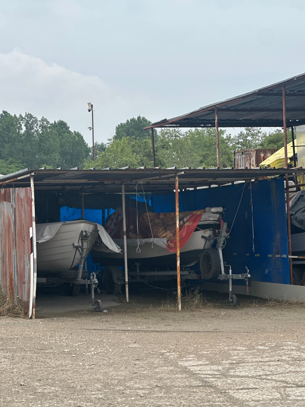 Boats in tarps stored at a waterfront lot, city skyline beyond
