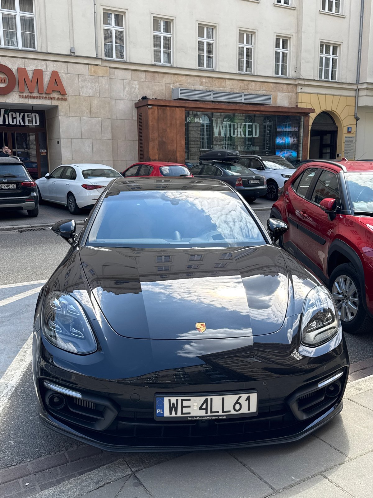 Black Porsche parked outside ROMA theater showing Wicked in Warsaw