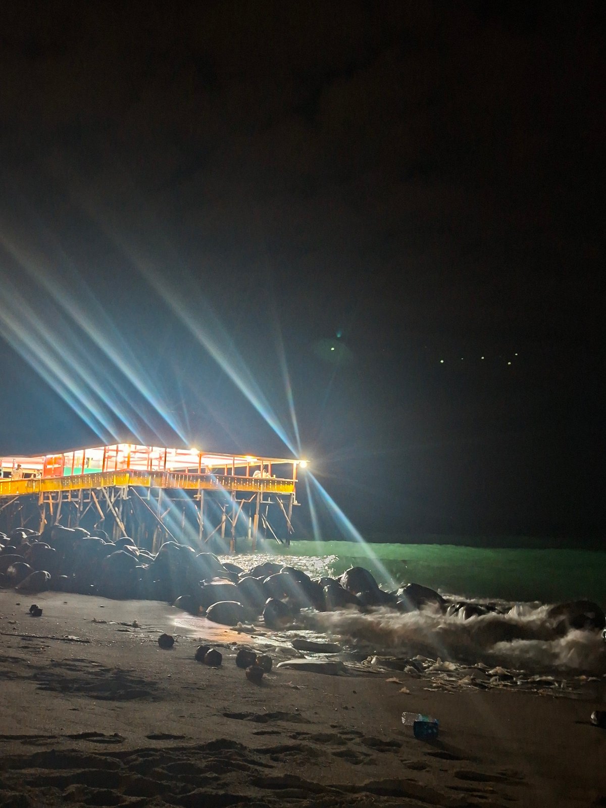 Illuminated pier captures attention during nighttime beach activity in Lhokseumawe