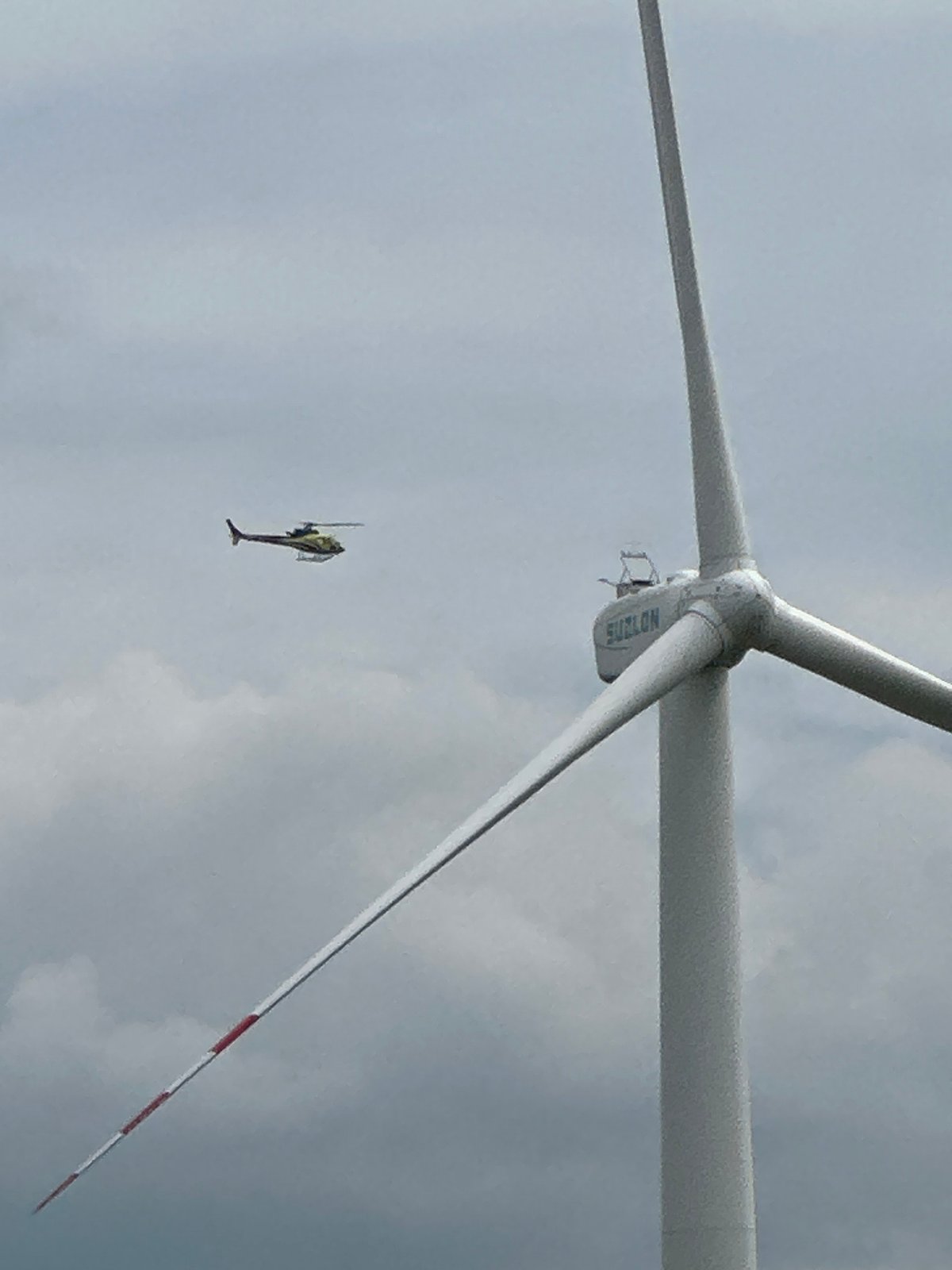 Yellow helicopter flies past wind turbine and comms tower in rural Ukraine