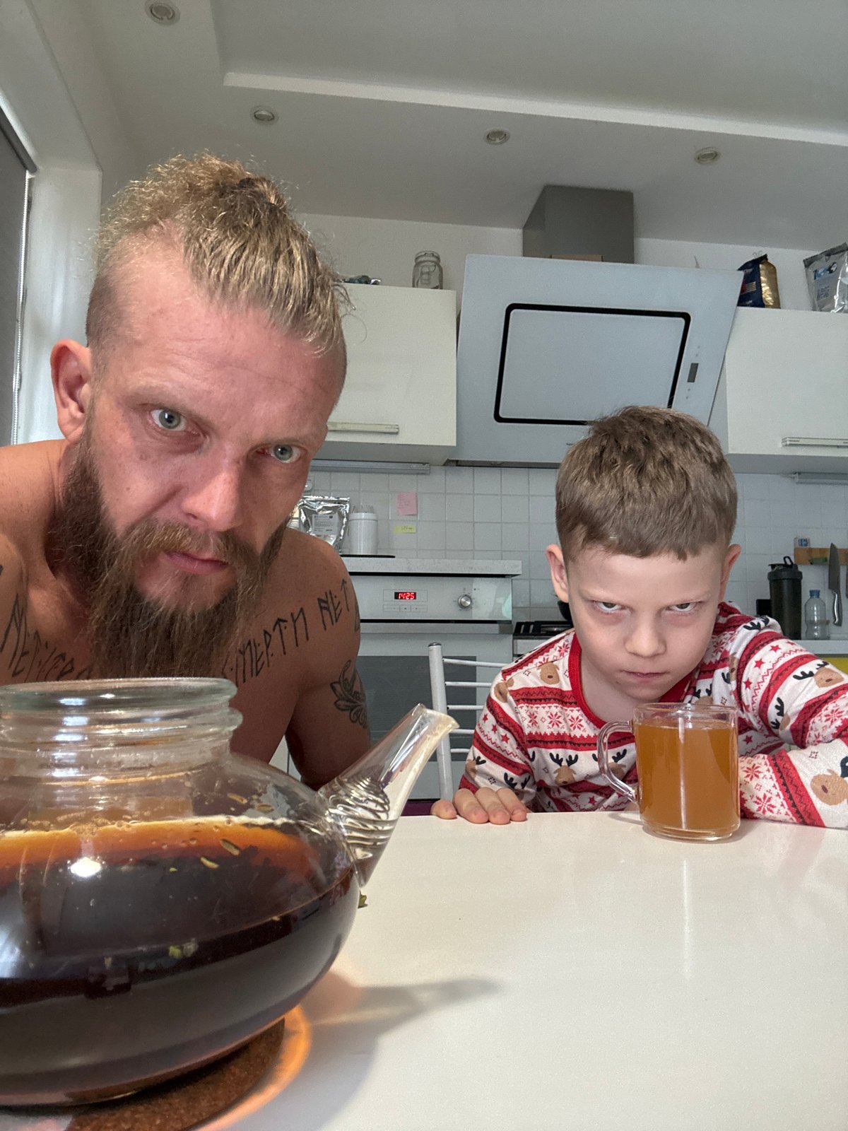 Tattooed man and boy share drinks in Volzhsky kitchen