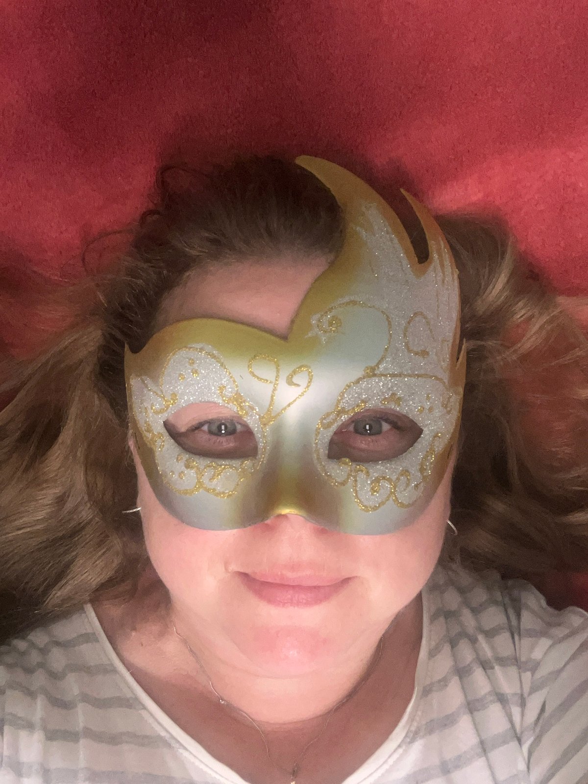 Masked portrait lying down against a vivid red backdrop.