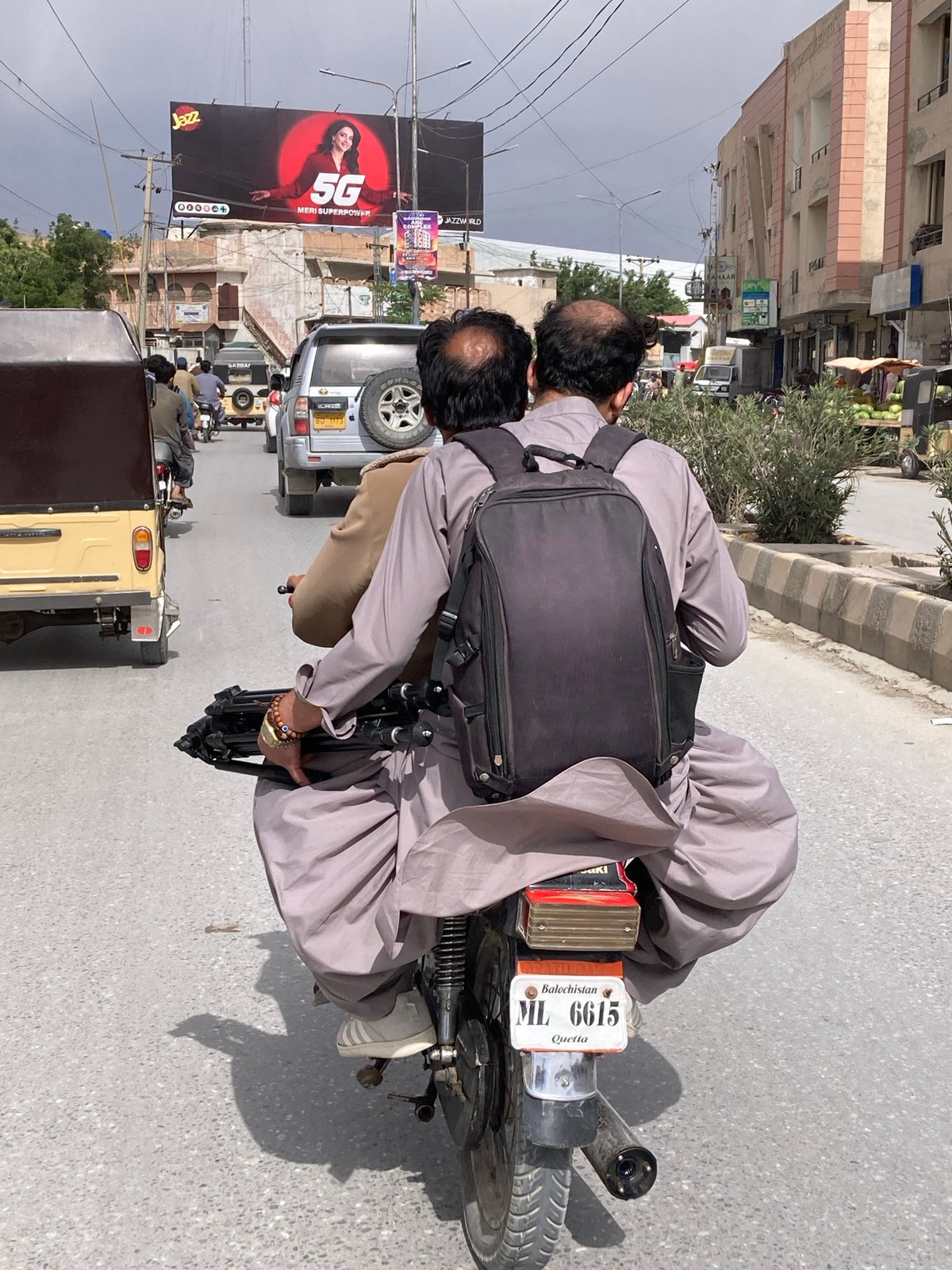 Two men ride motorcycle through Quetta streets under overcast sky