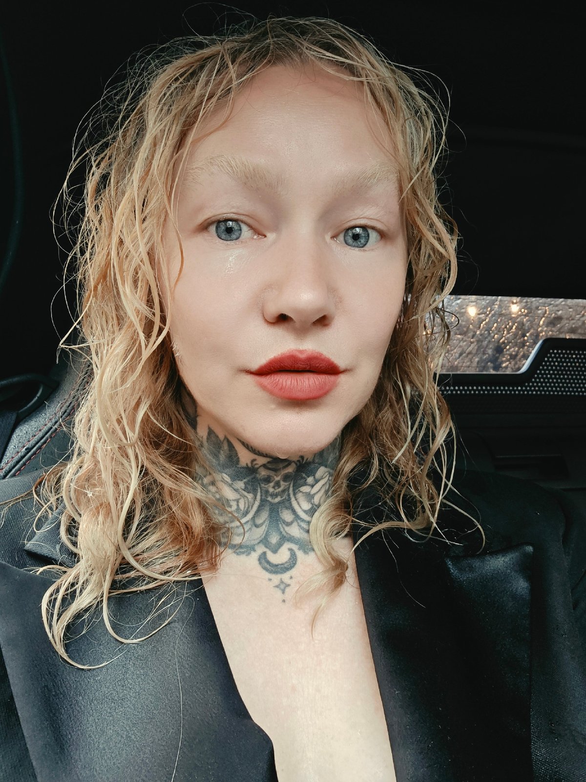 Wet hair, neck tattoos, black blazer — direct eye contact in St. Petersburg