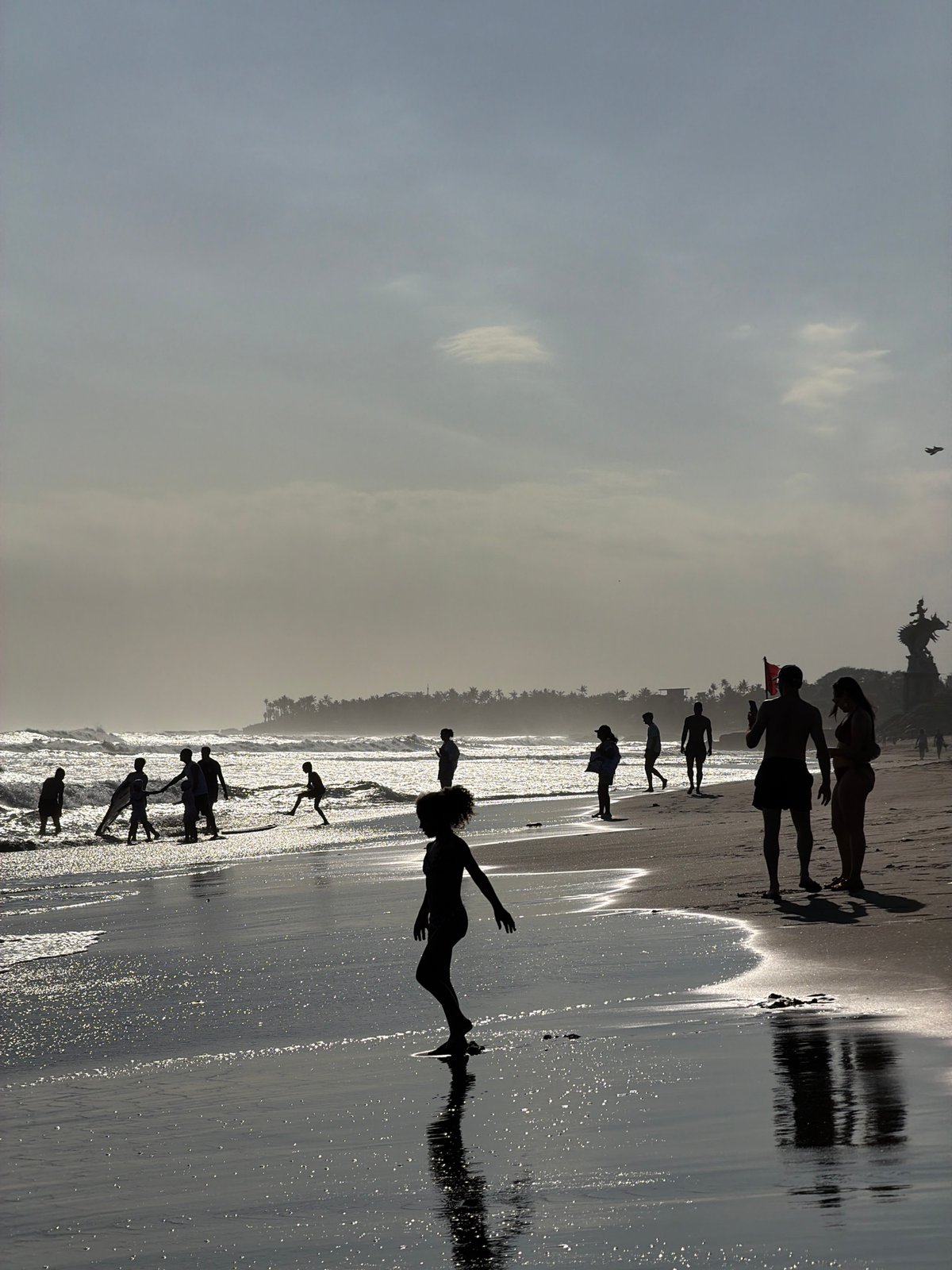 Surfers and beachgoers fill a hazy North Kuta morning