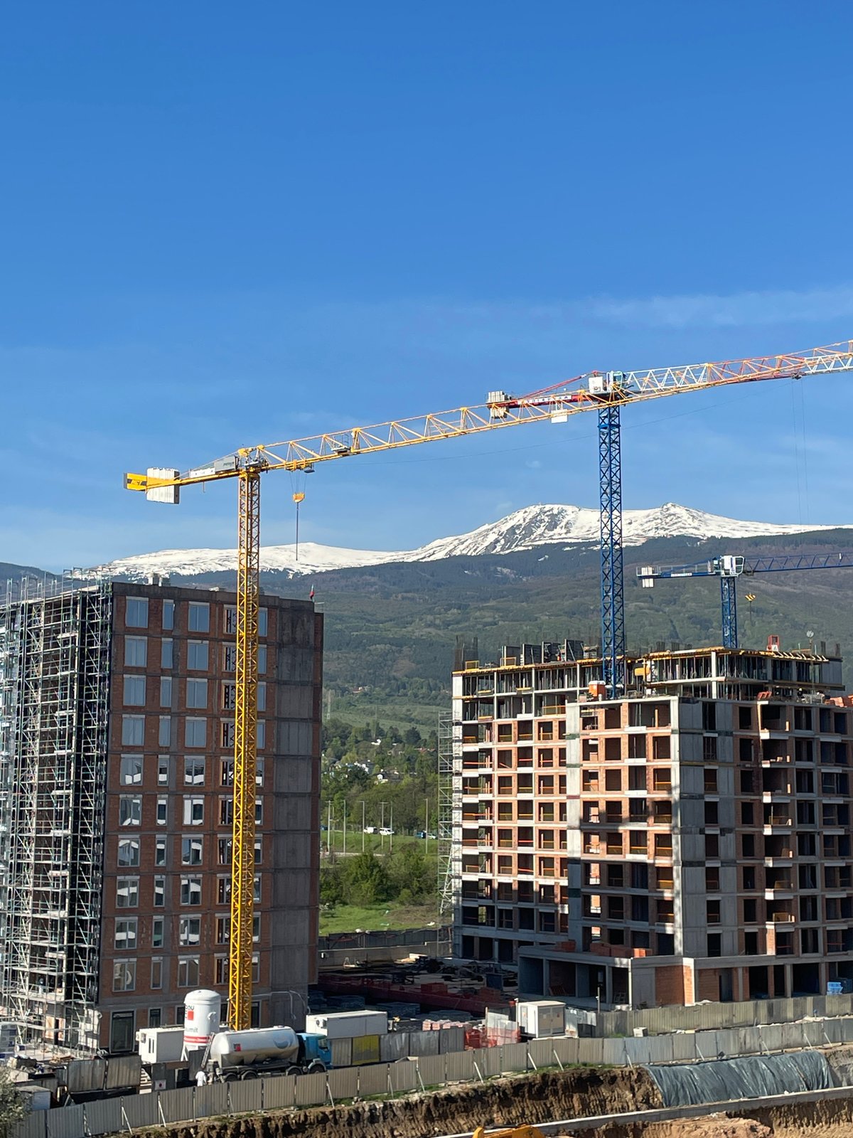 Construction cranes operate at Sofia building site against mountain backdrop