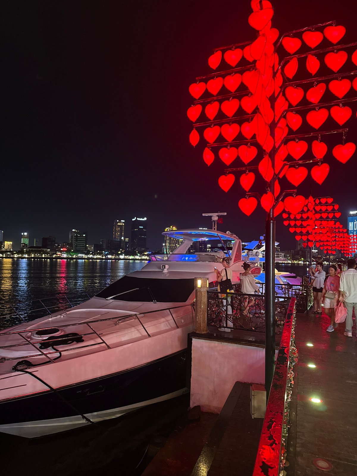 Nighttime festivities along Đà Nẵng waterfront feature heart lanterns, yacht