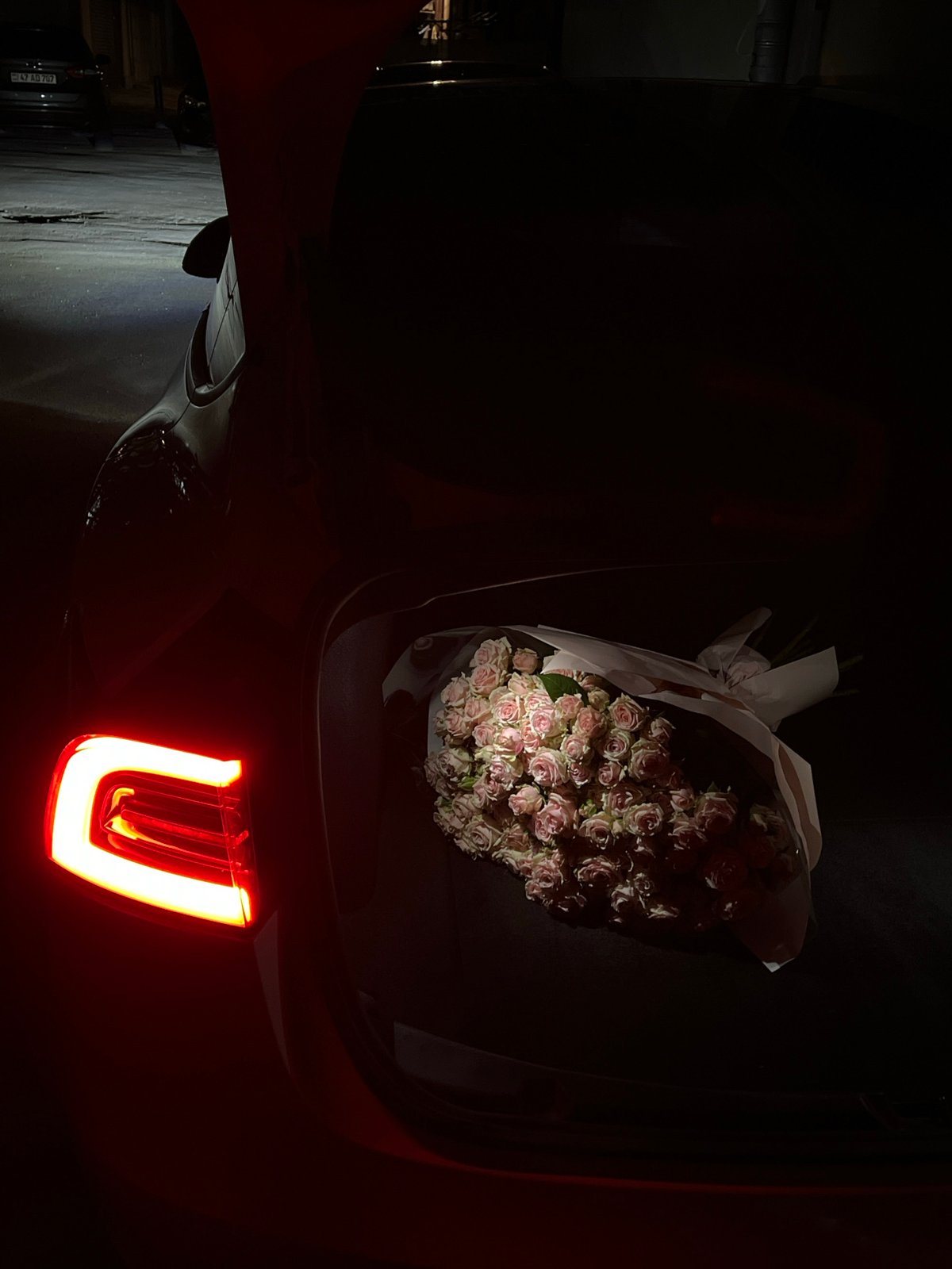 Pink roses left on car trunk in nighttime Yerevan