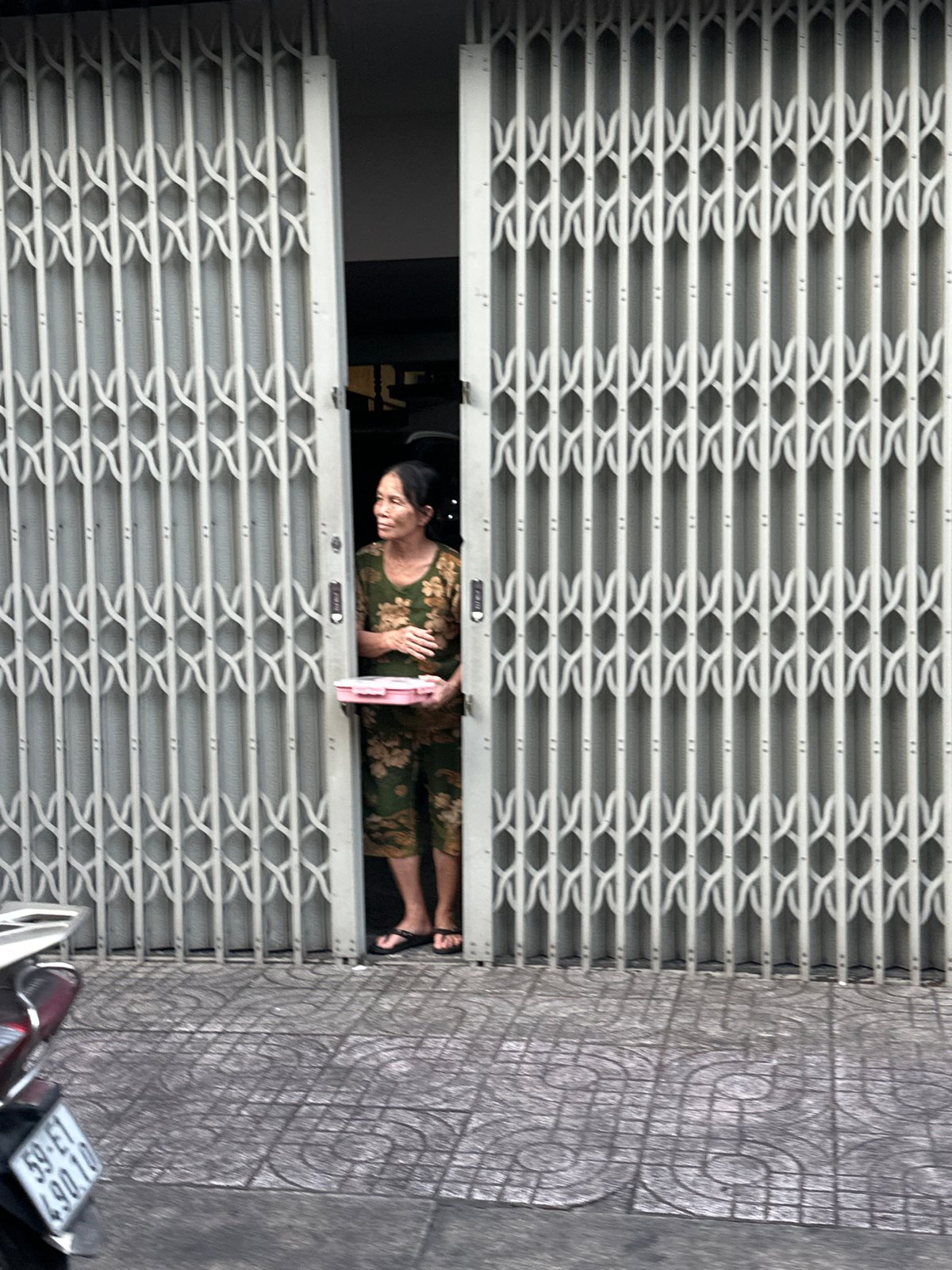 Man sits on parked moped near grid door in Thủ Đức