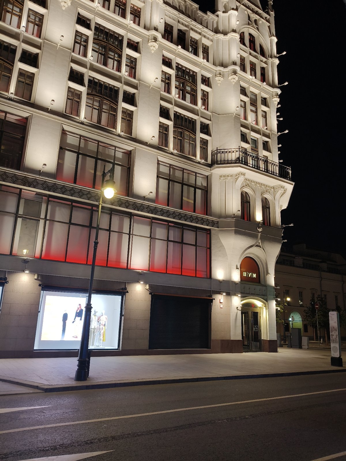 Grand classical building at night, banners and storefronts nearby