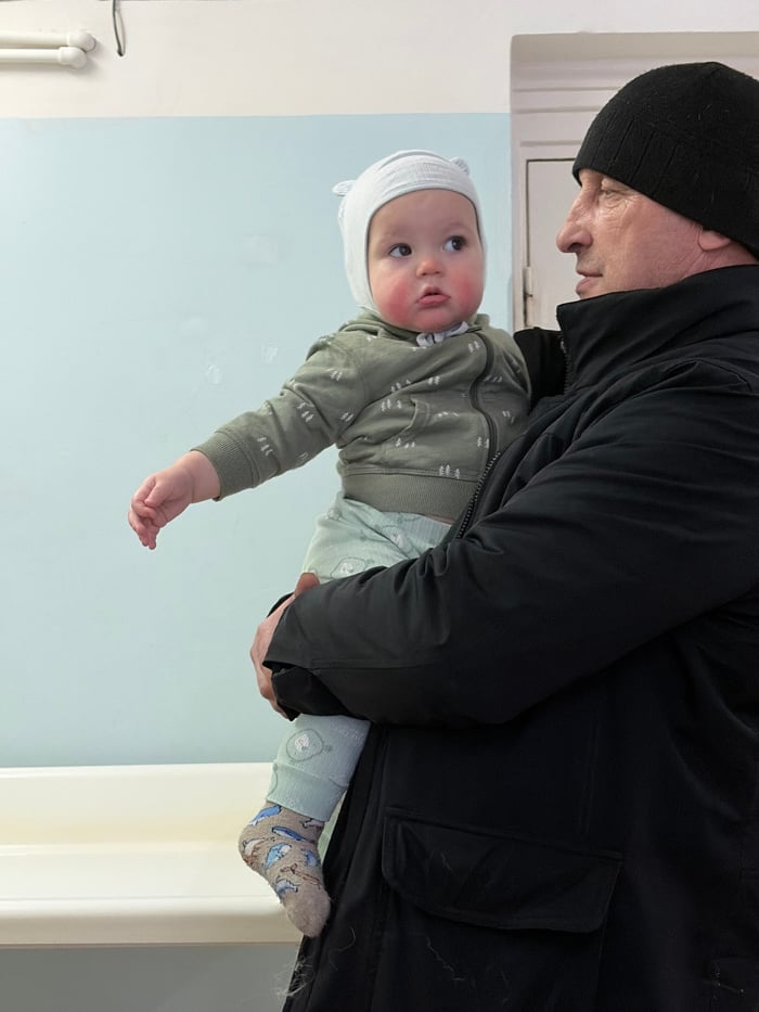 Adult holds baby indoors during Russian winter morning