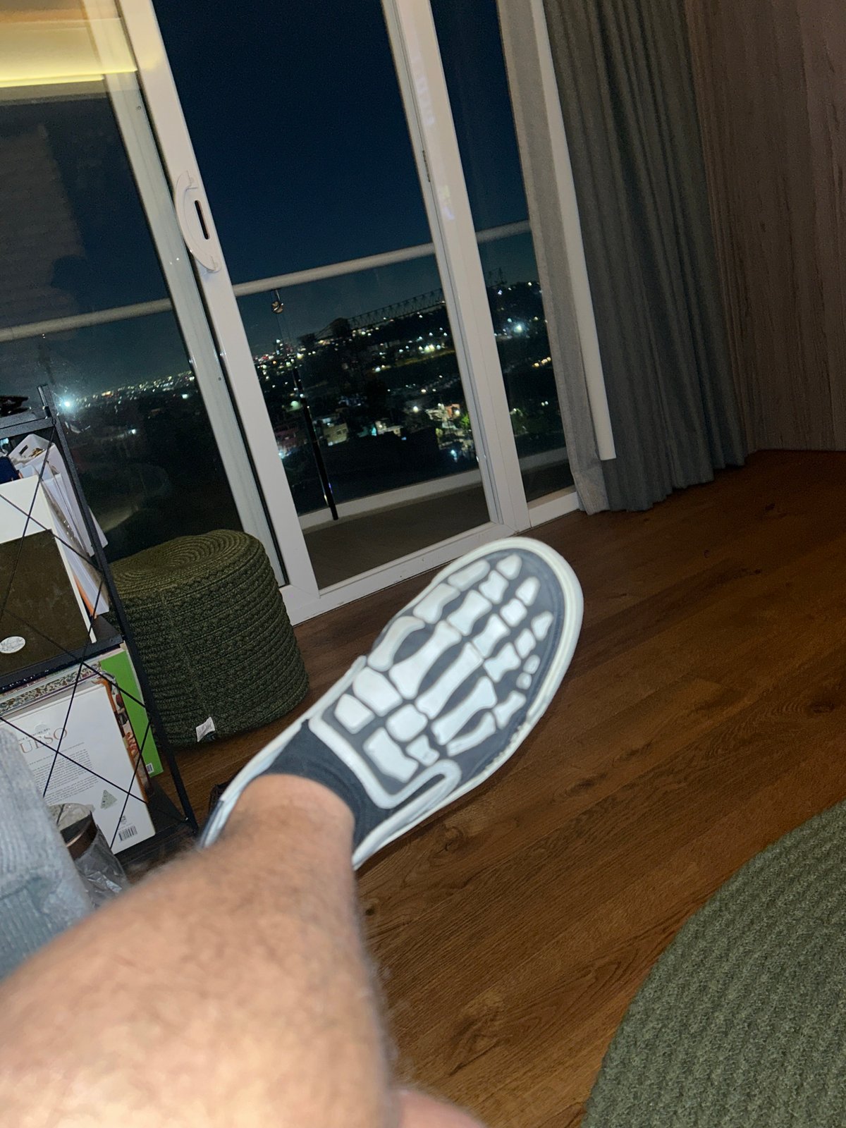 Person photographed by window in Huixquilucan wearing skeleton-print shoes