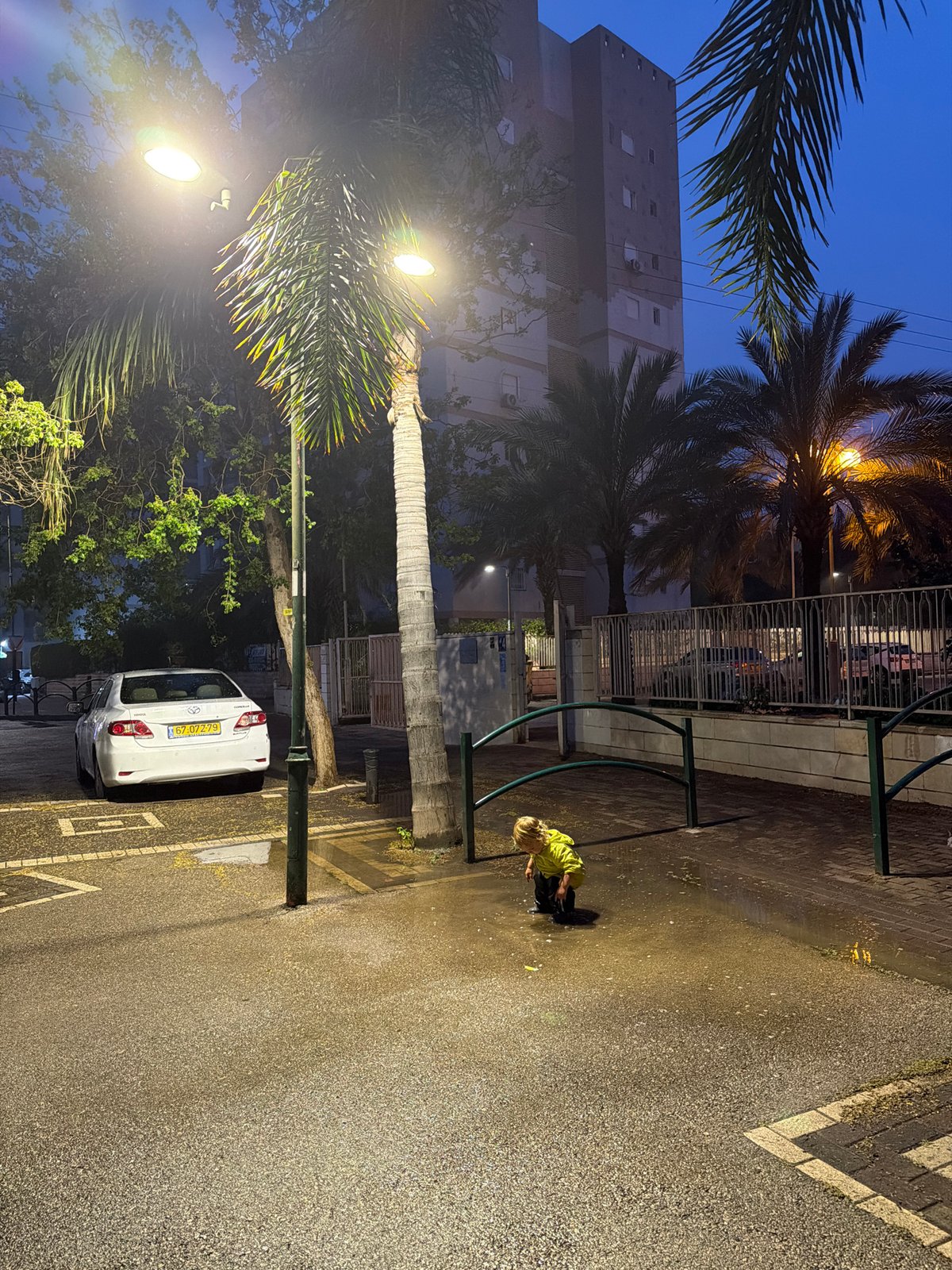 Child plays in wet Kiryat Bialik square at dusk