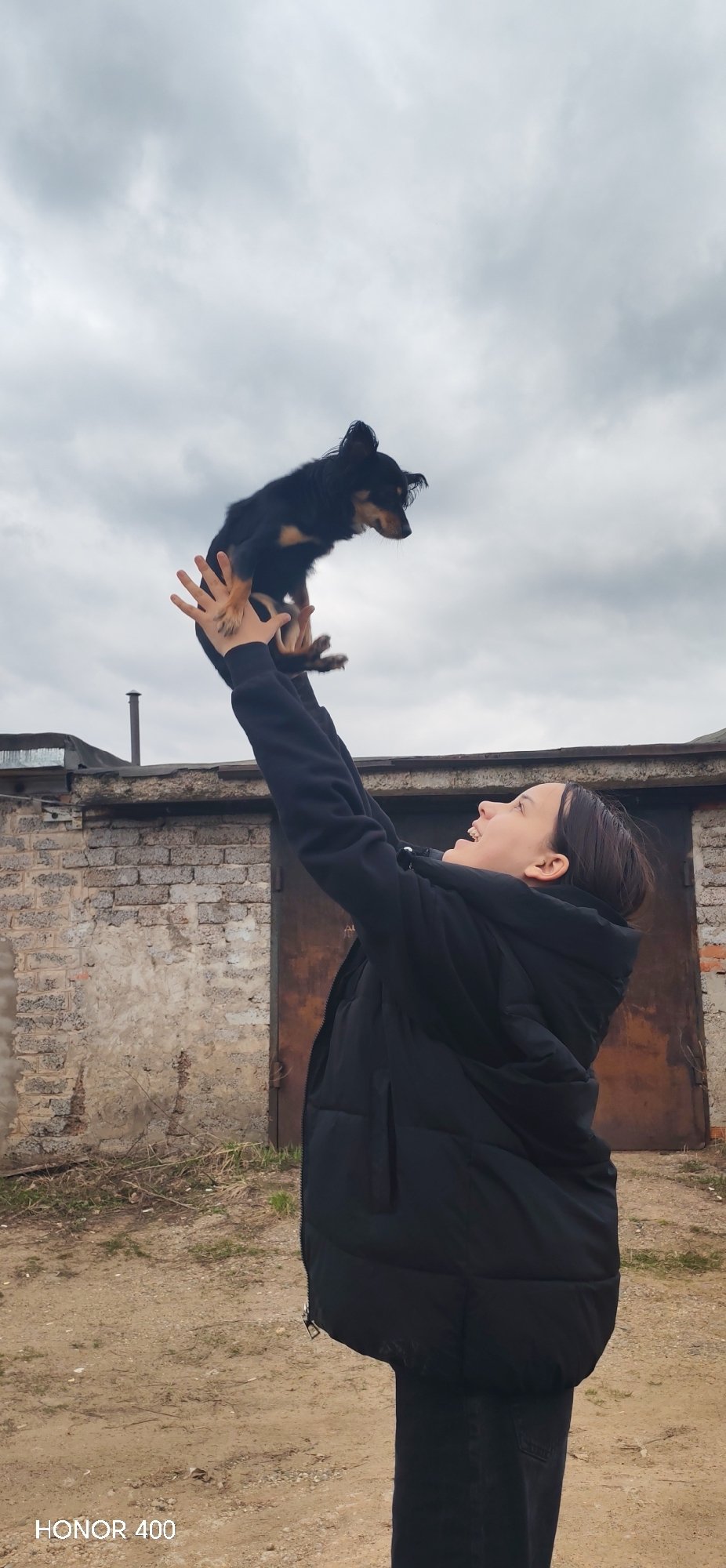 Woman plays with small dog outside garages in Noviy, Russia