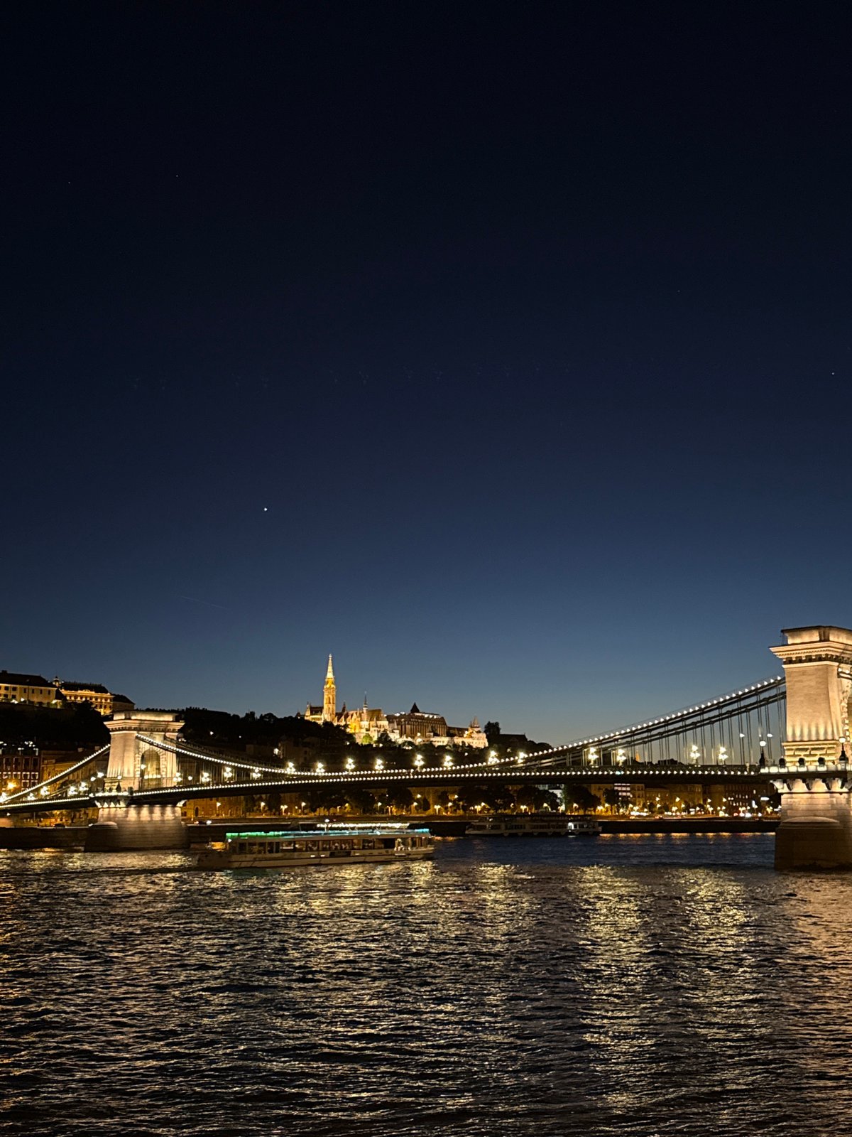 Budapest Chain Bridge illuminated at night, boats passing beneath