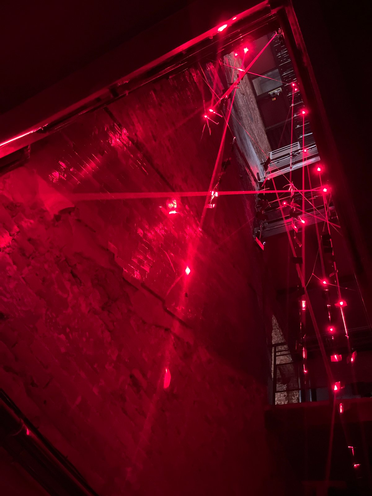 Red-lit installation space with lasers, crowds, and theatrical projections