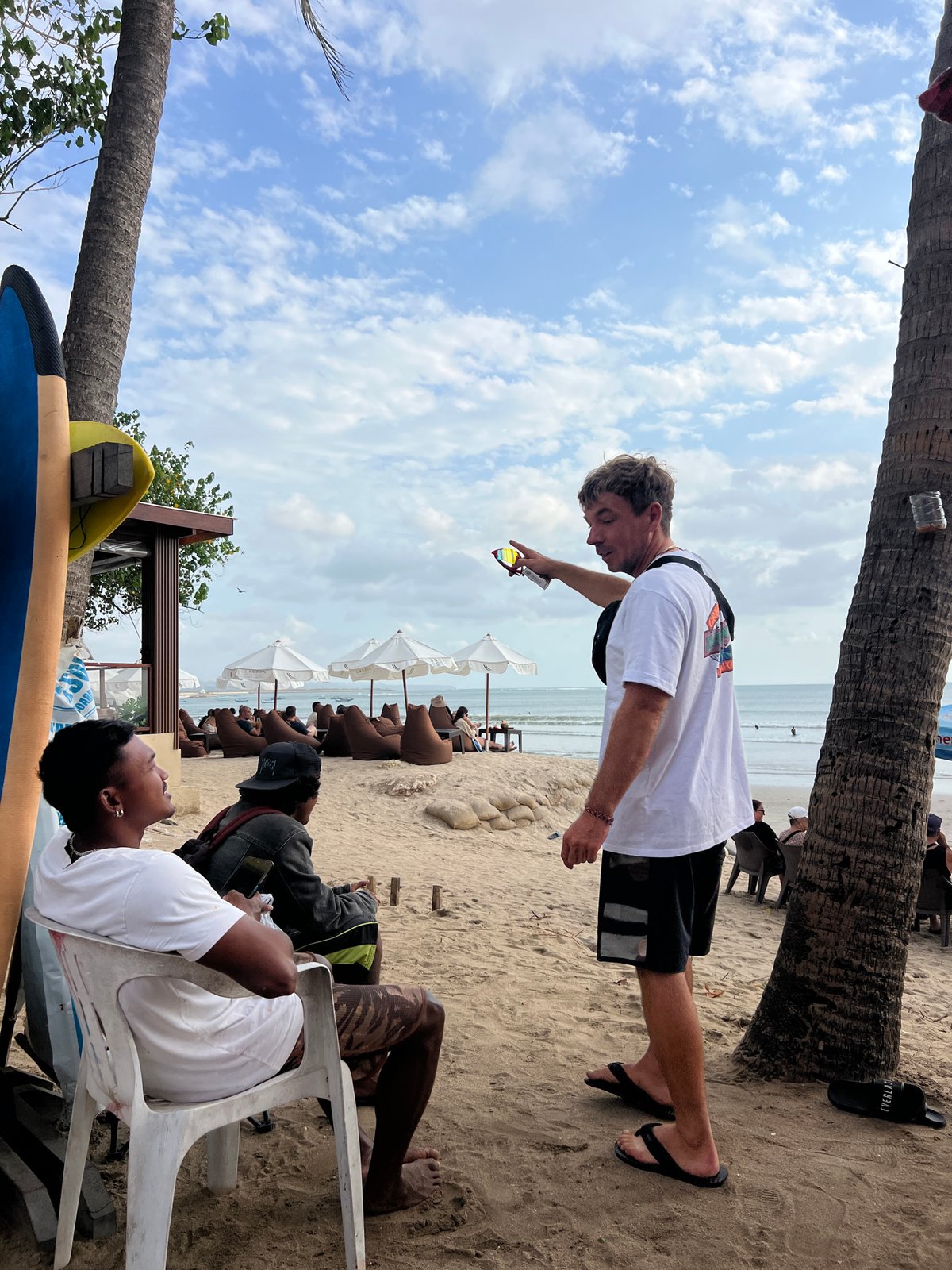 Lazy morning at Kuta Beach with umbrellas, surfers, and shoreline crowds.