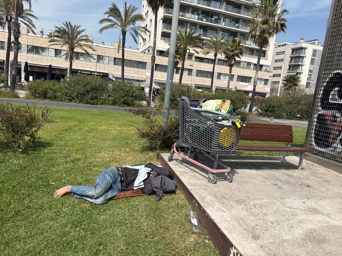 Children skate while homeless man rests at Barcelona waterfront park