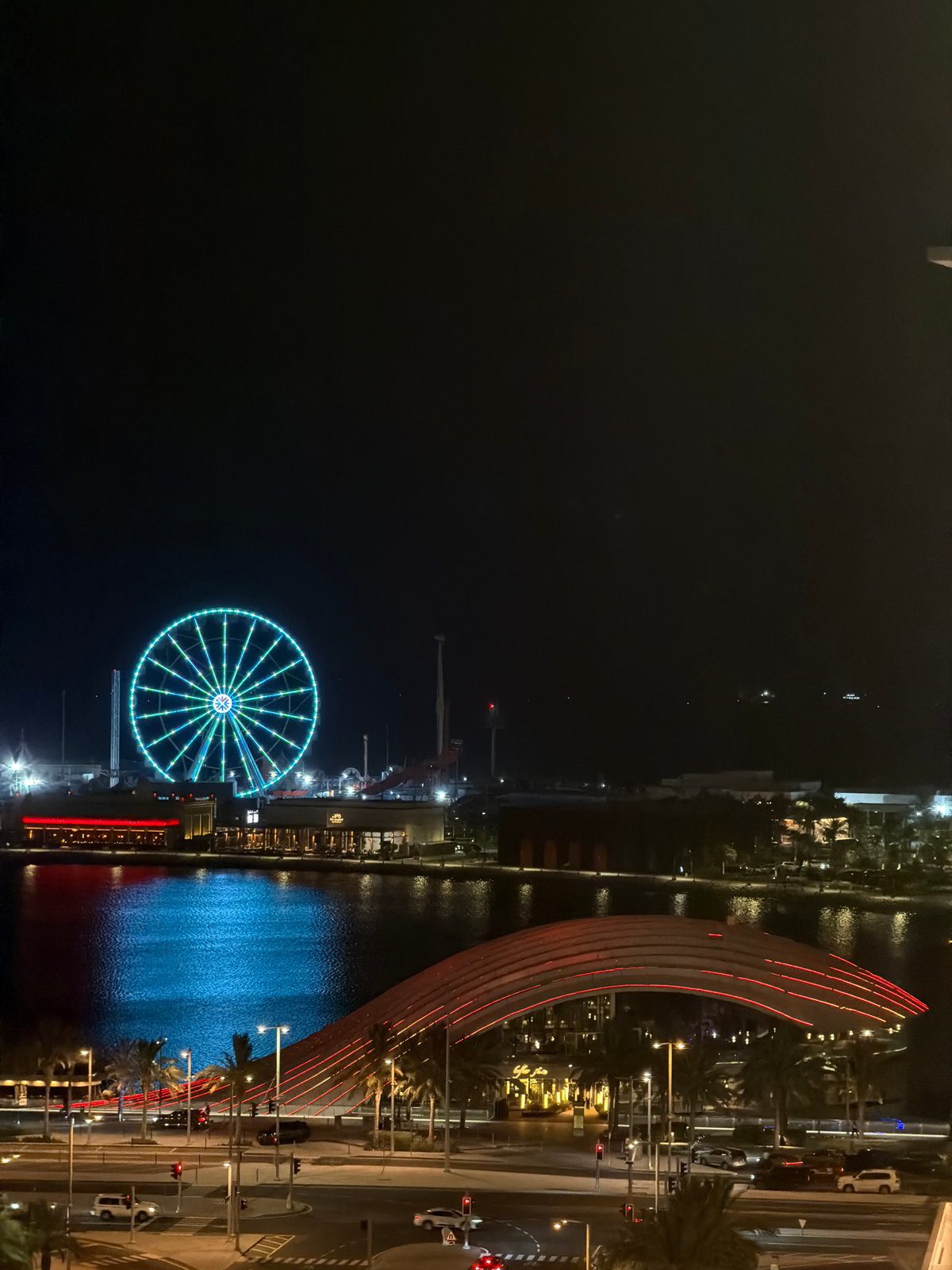 Illuminated Ferris wheel anchors a busy urban waterfront at night