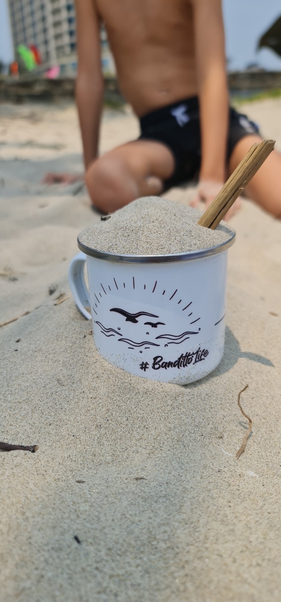 Child plays with sand-filled mug on Đà Nẵng beach