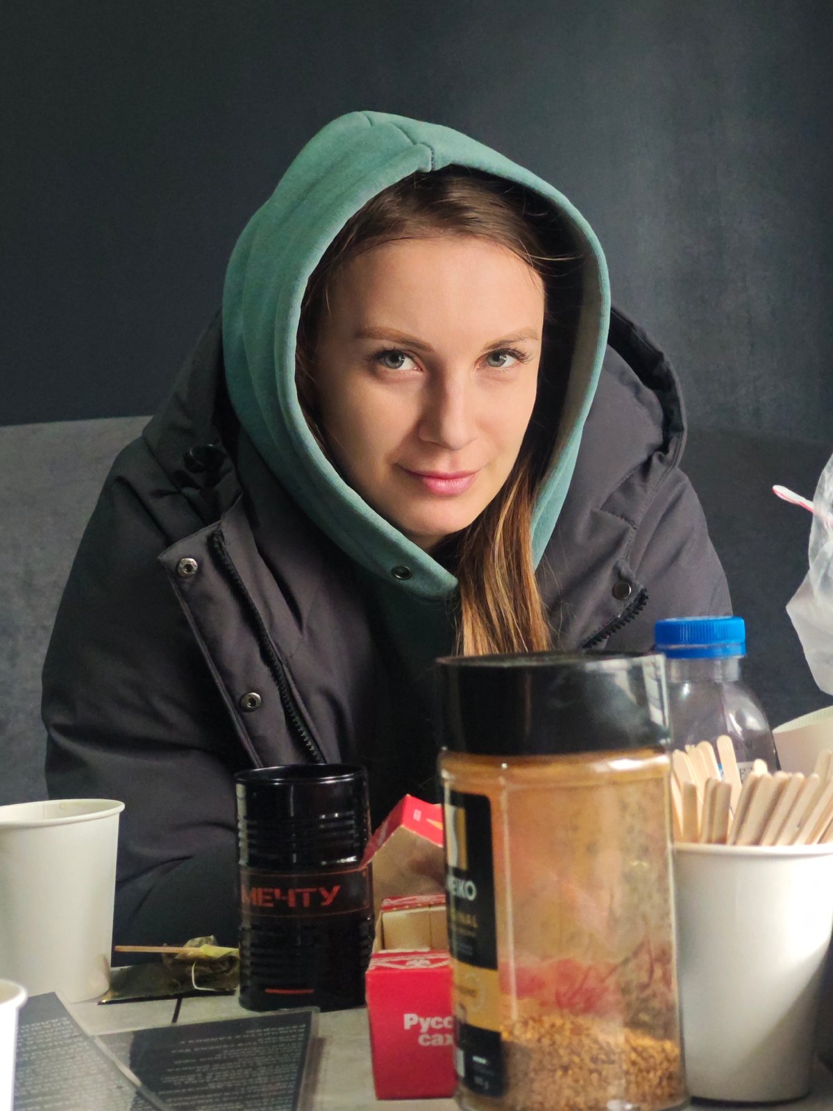 Young woman in green hoodie sits at cluttered table