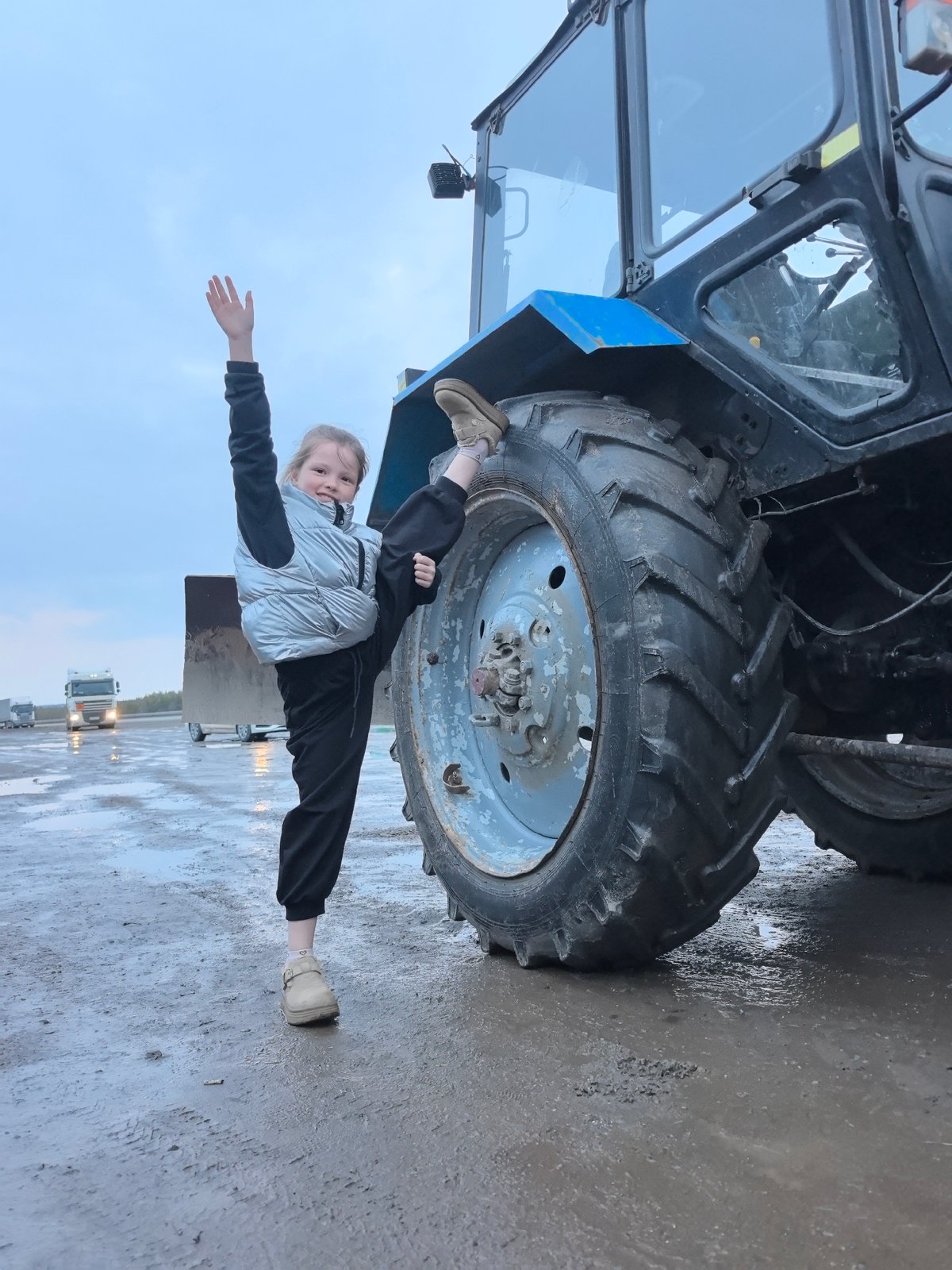 Girl performs gymnastic splits near farm vehicles in Russia