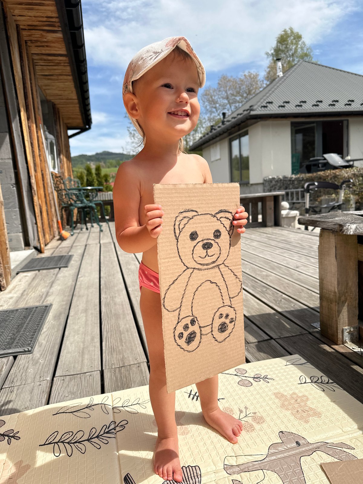 Toddler displays teddy bear drawing on deck in Wisła