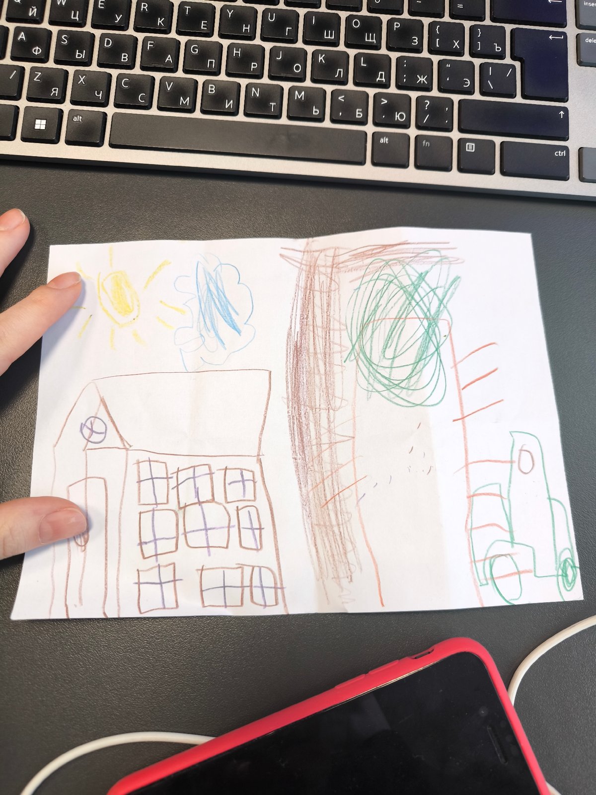 Child's Drawing Displayed on Surface Near Laptop, Hand Points
