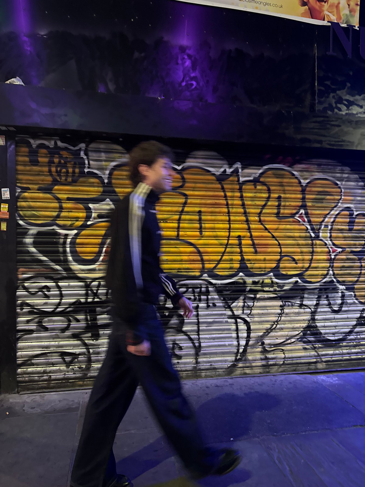 Night scene captures person moving past graffitied London shutter