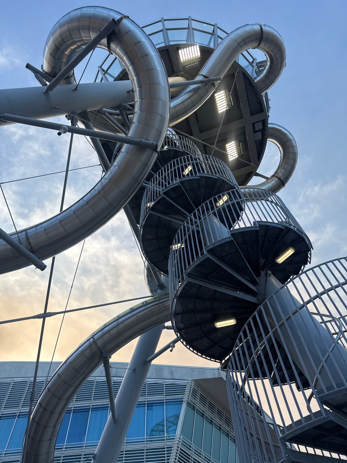 Massive metallic spiral slide structure photographed from below at dusk