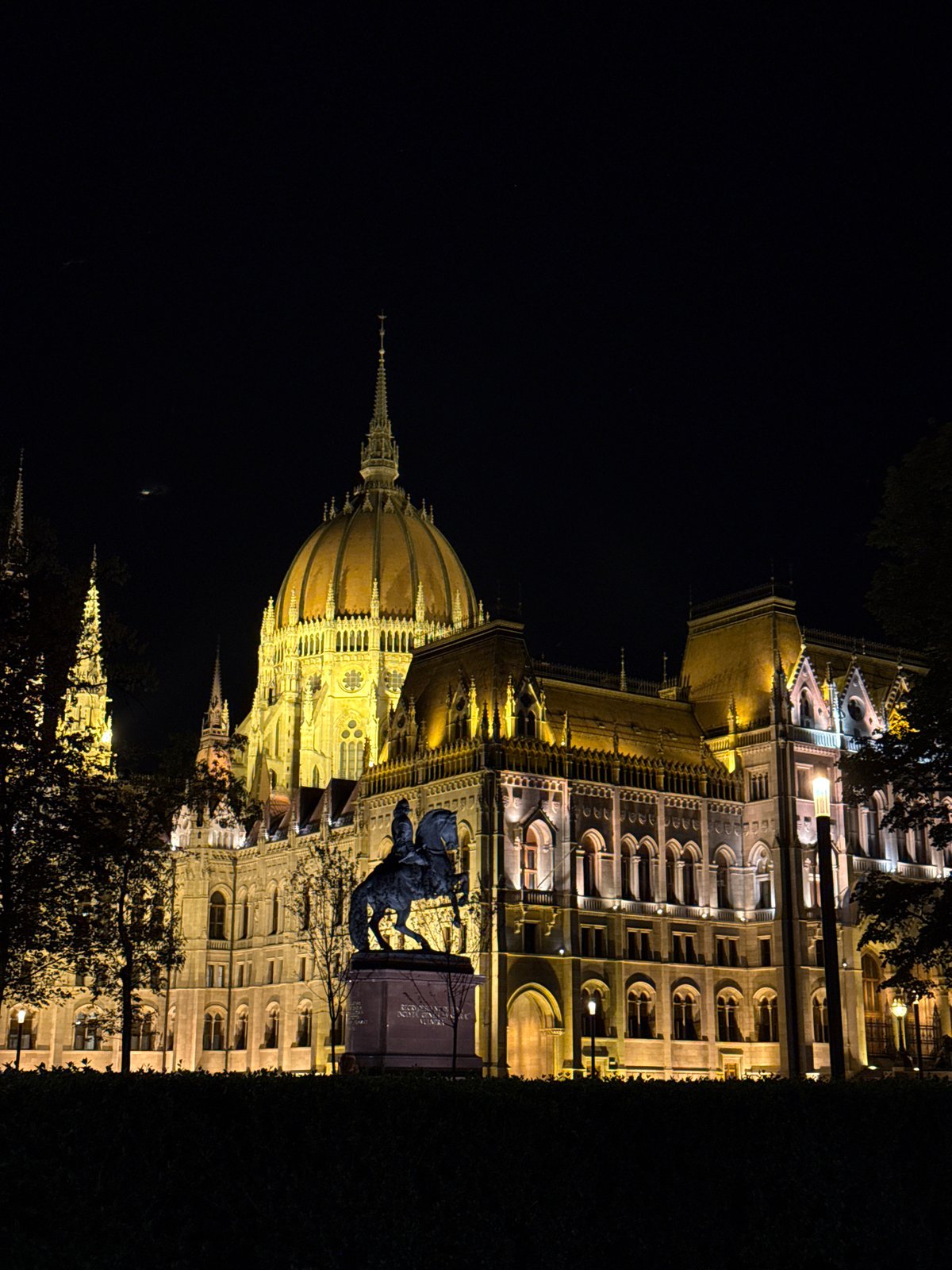 Tourists photograph illuminated Hungarian Parliament Building at night in Budapest