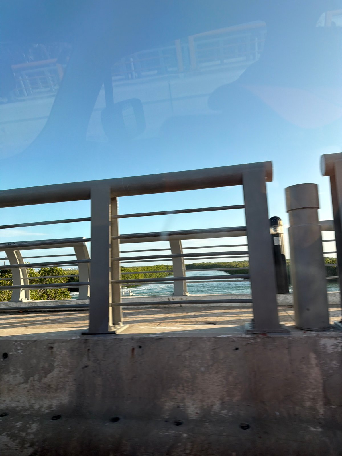 Vehicle passenger observes waterside railing and foliage in Cancún
