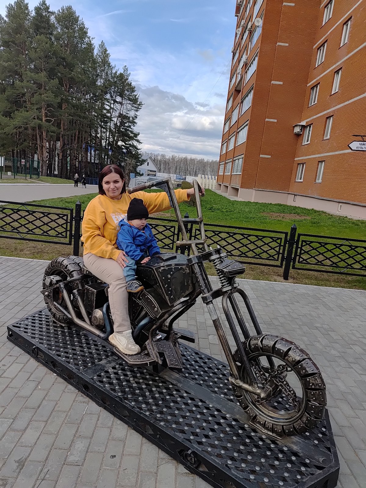 Woman and child pose on motorcycle sculpture in Chaikovsky