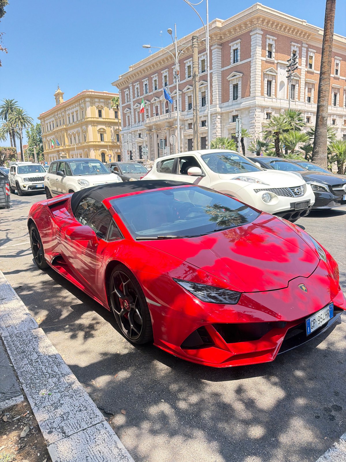 Red Lamborghini and Fiat Topolino parked on sunny Bari street